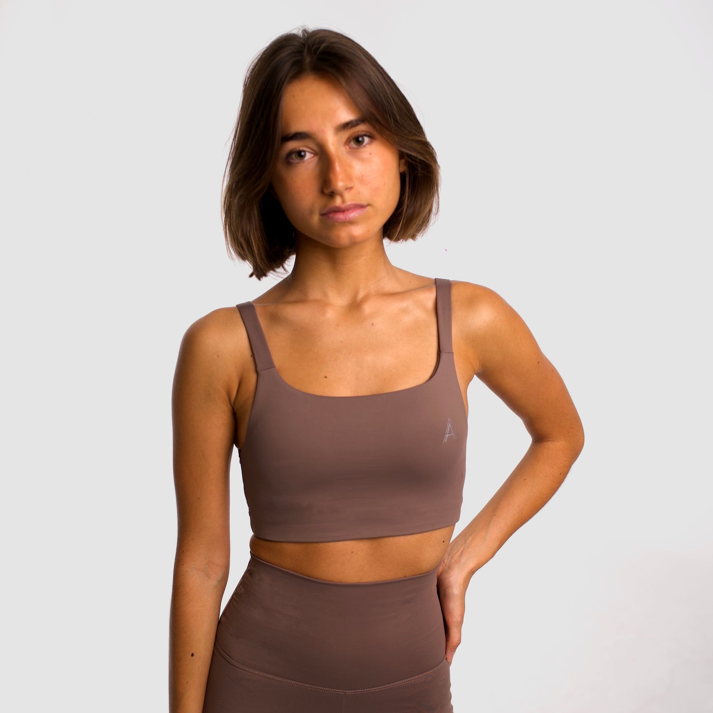 Women's camel sports top. Cross-strap bra. Elastic chest strap for comfort and support. Lightweight, breathable and comfortable bra. Removable cups. Top deportivo de mujer beige. Sujetador de tirantes cruzados. Tira elástica en el pecho ofreciendo comodidad y sujeción. Sujetador cómo, ligero y transpirable. Top con copas extraibles.