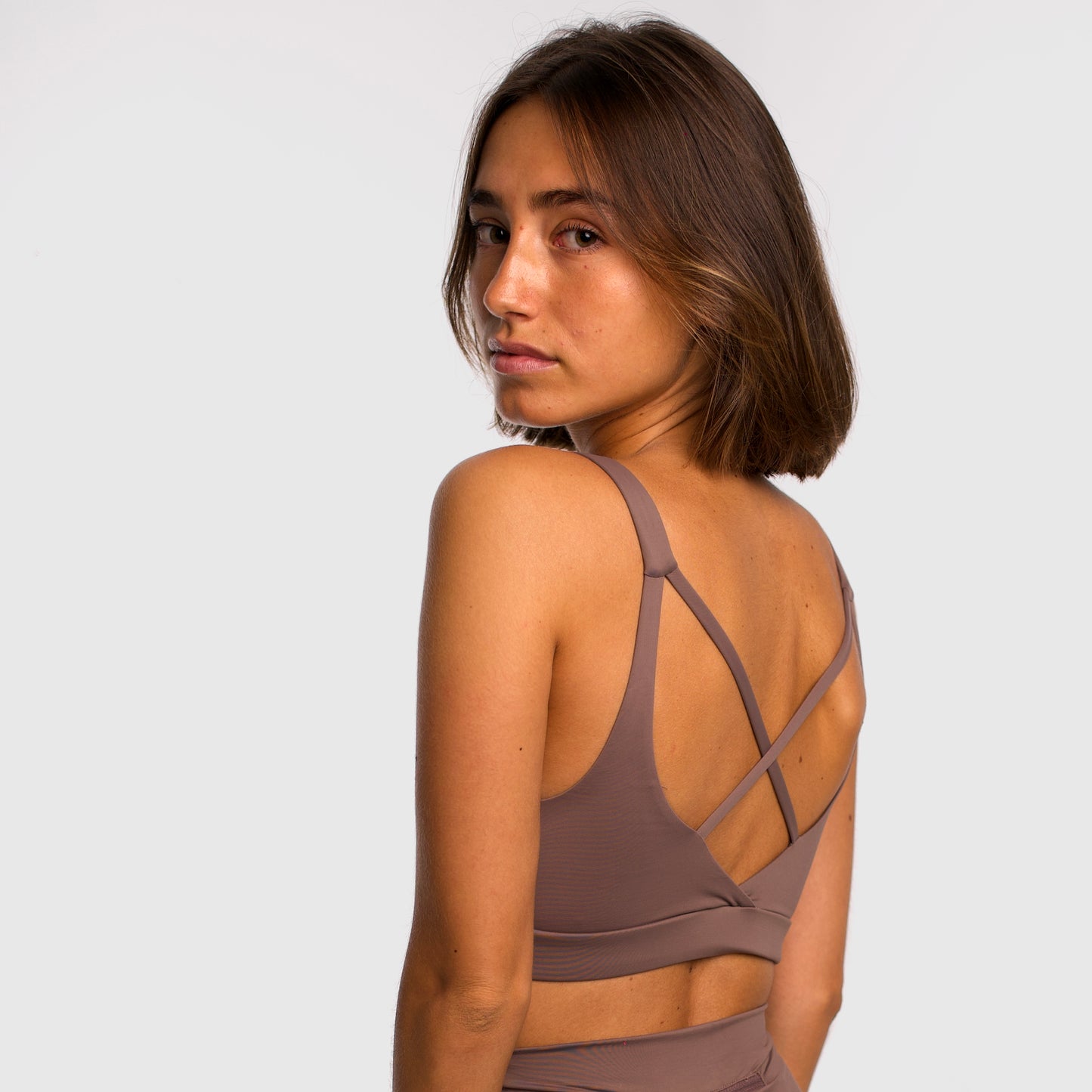 Women's camel sports top. Cross-strap bra. Elastic chest strap for comfort and support. Lightweight, breathable and comfortable bra. Removable cups. Top deportivo de mujer beige. Sujetador de tirantes cruzados. Tira elástica en el pecho ofreciendo comodidad y sujeción. Sujetador cómo, ligero y transpirable. Top con copas extraibles. 