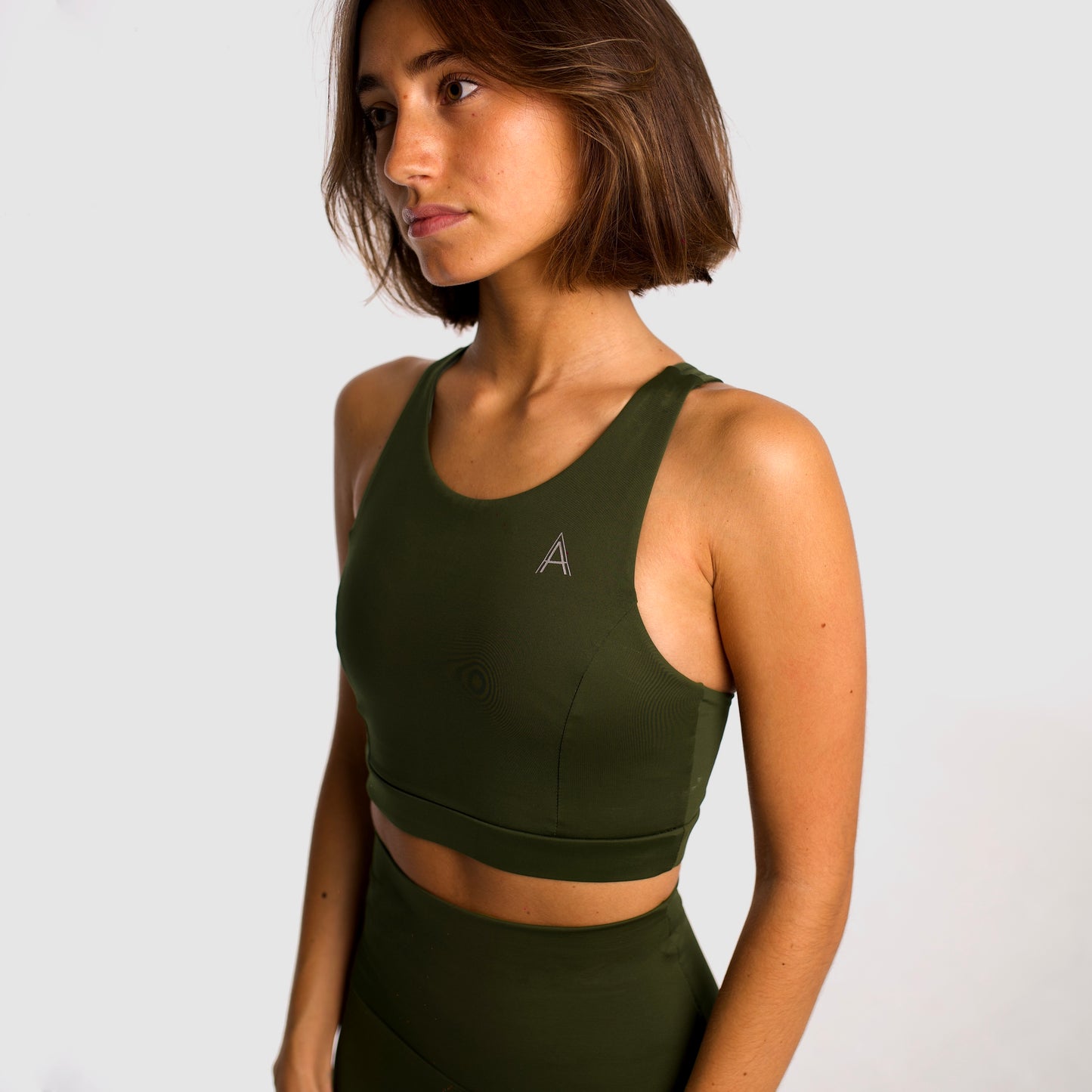 Women's khaki sports top. Long cut bra. Elastic chest strap for comfort and support. Lightweight, breathable and comfortable bra. Removable cups. Top deportivo de mujer color khaki. Sujetador de corte largo. Tira elástica en el pecho ofreciendo comodidad y sujeción. Sujetador cómo, ligero y transpirable. Top con copas extraibles. 