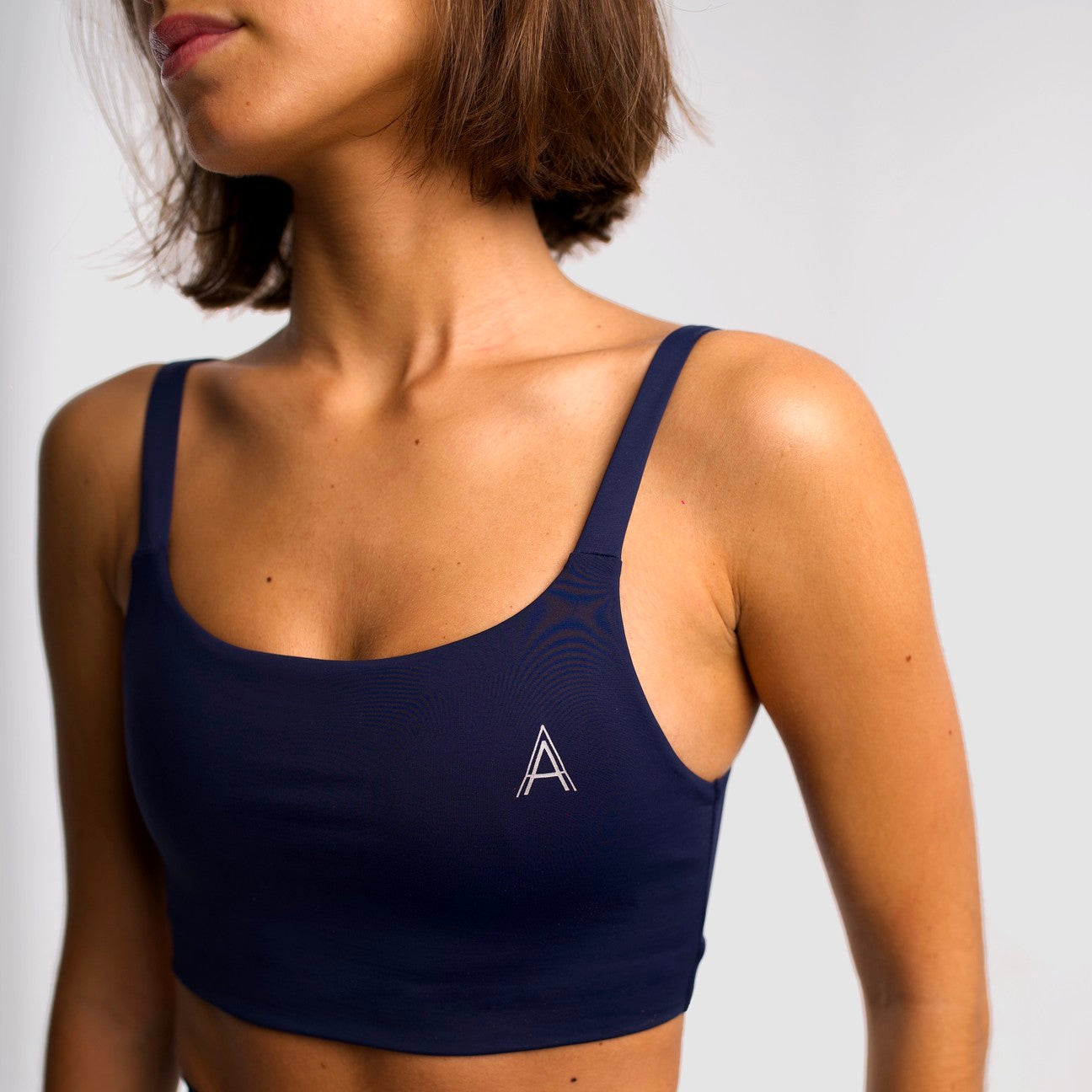 Women's navy blue sports top. Cross-strap bra. Elastic chest strap for comfort and support. Lightweight, breathable and comfortable bra. Removable cups. Top deportivo de mujer azul marino. Sujetador de tirantes cruzados. Tira elástica en el pecho ofreciendo comodidad y sujeción. Sujetador cómo, ligero y transpirable. Top con copas extraibles. 