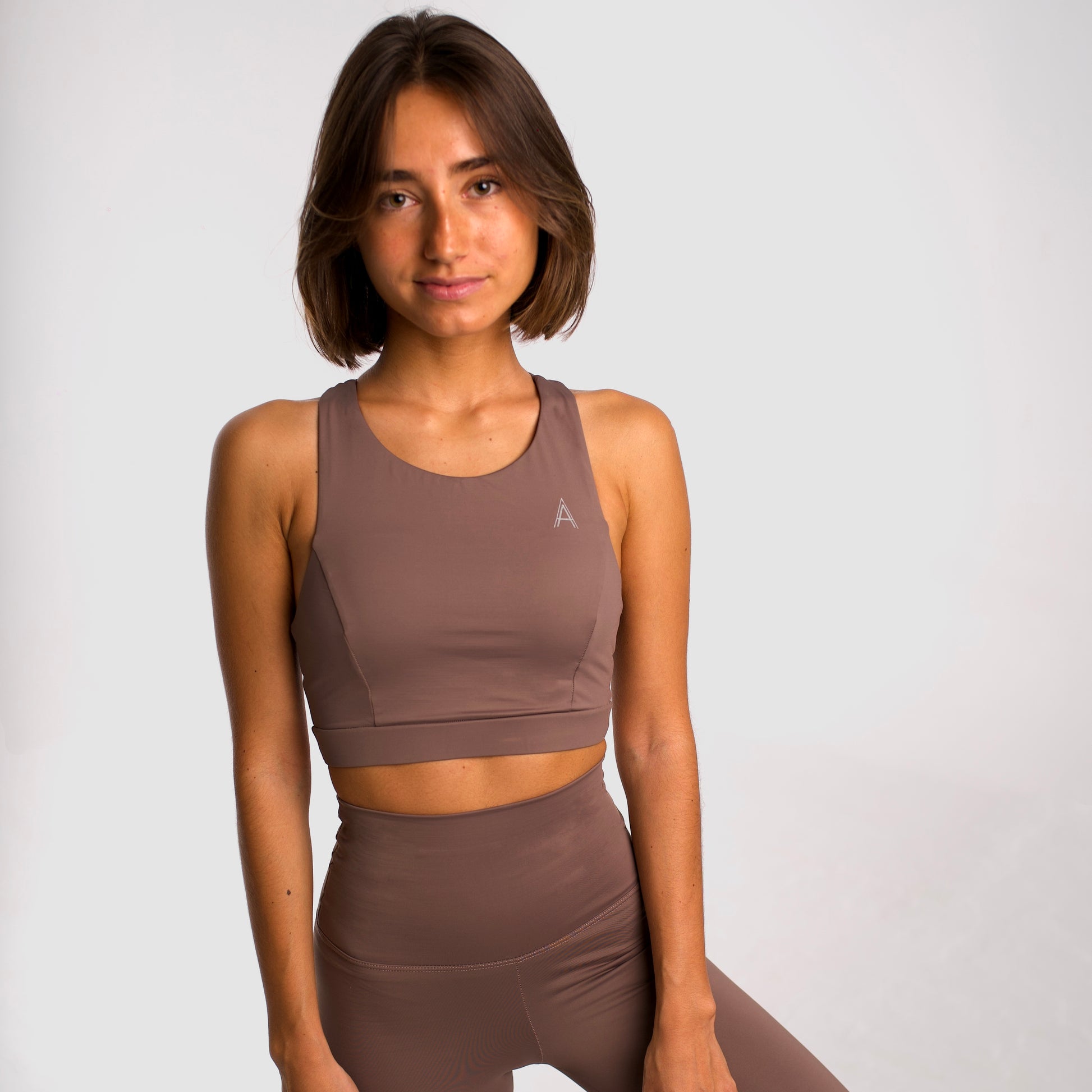 Women's beige sports top. Long cut bra. Elastic chest strap for comfort and support. Lightweight, breathable and comfortable bra. Removable cups. Top deportivo de mujer color beige. Sujetador de corte largo. Tira elástica en el pecho ofreciendo comodidad y sujeción. Sujetador cómo, ligero y transpirable. Top con copas extraibles. 