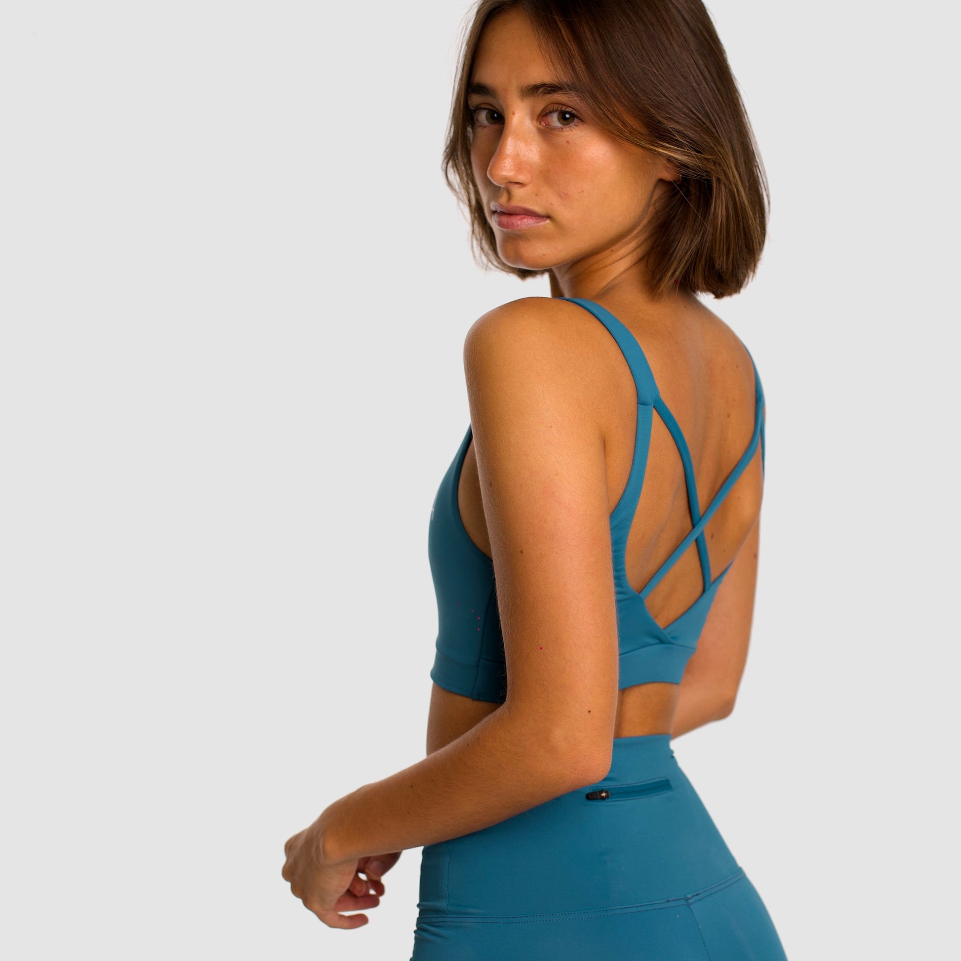 Women's canard blue sports bra. Cross-strap bra. Lightweight, breathable and comfortable bra. Removable cups. Top deportivo de mujer azul pato. Sujetador de tirantes cruzados. Tira elástica en el pecho ofreciendo comodidad y sujeción. Sujetador cómodo, ligero y transpirable. Top con copas extraíbles. 