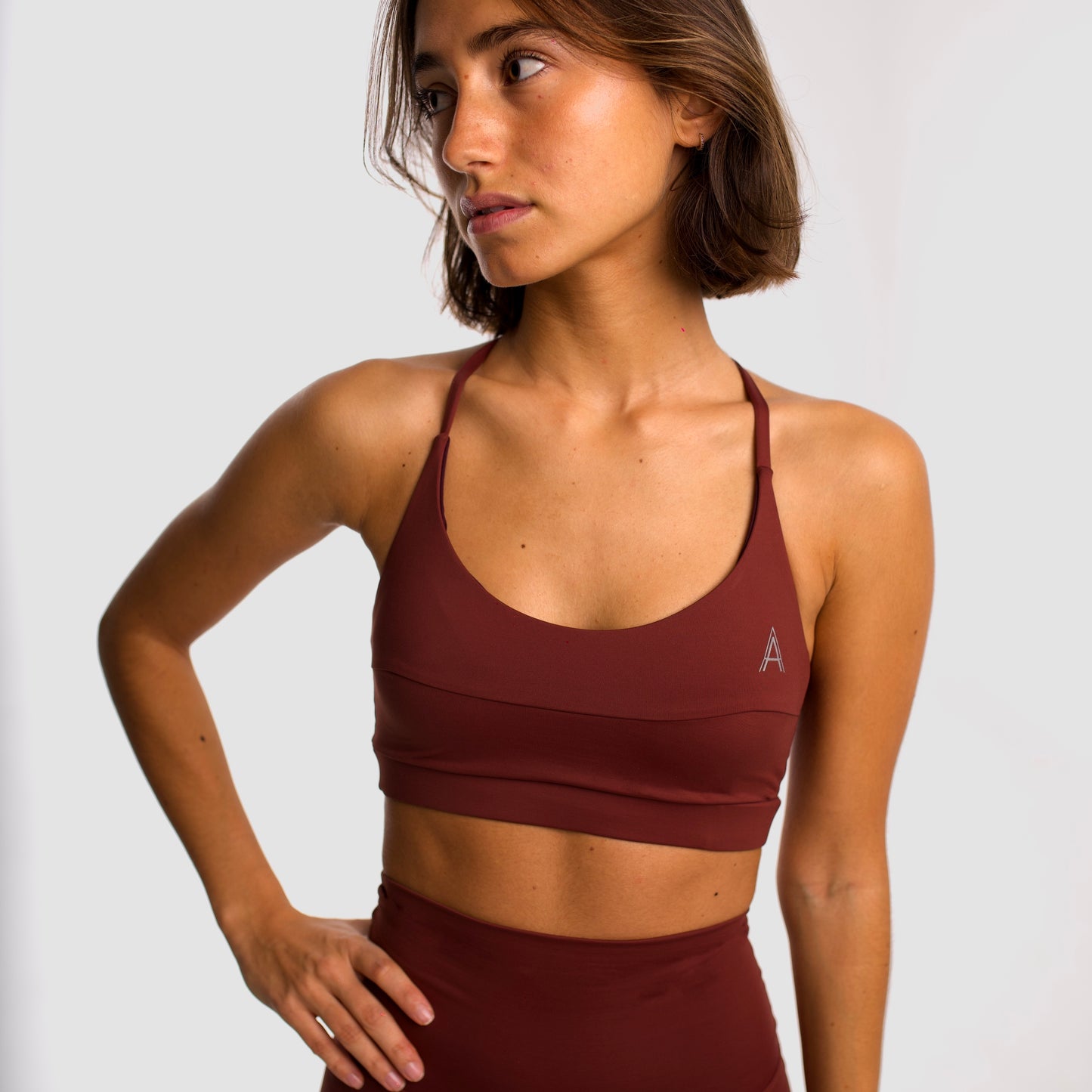 Women's maroon sports top. Cross-strap bra. Elastic chest strap for comfort and support. Lightweight, breathable and comfortable bra. Removable cups. Top Deportivo mujer color granate. Sujetador de tirantes cruzados. Tira elástica en el pecho ofreciendo comodidad y sujeción. Sujetador cómo, ligero y transpirable. Top con copas extraibles.