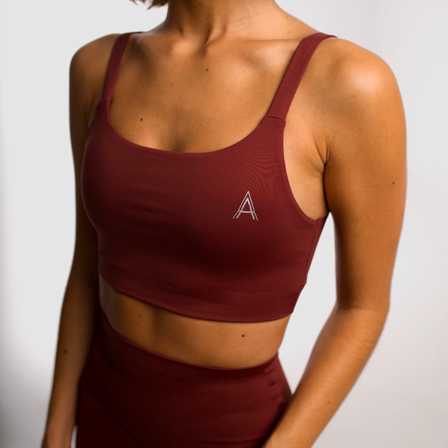 Women's maroon sports top. Cross-strap bra. Elastic chest strap for comfort and support. Lightweight, breathable and comfortable bra. Removable cups. Top deportivo de mujer granate. Sujetador de tirantes cruzados. Tira elástica en el pecho ofreciendo comodidad y sujeción. Sujetador cómo, ligero y transpirable. Top con copas extraibles. 