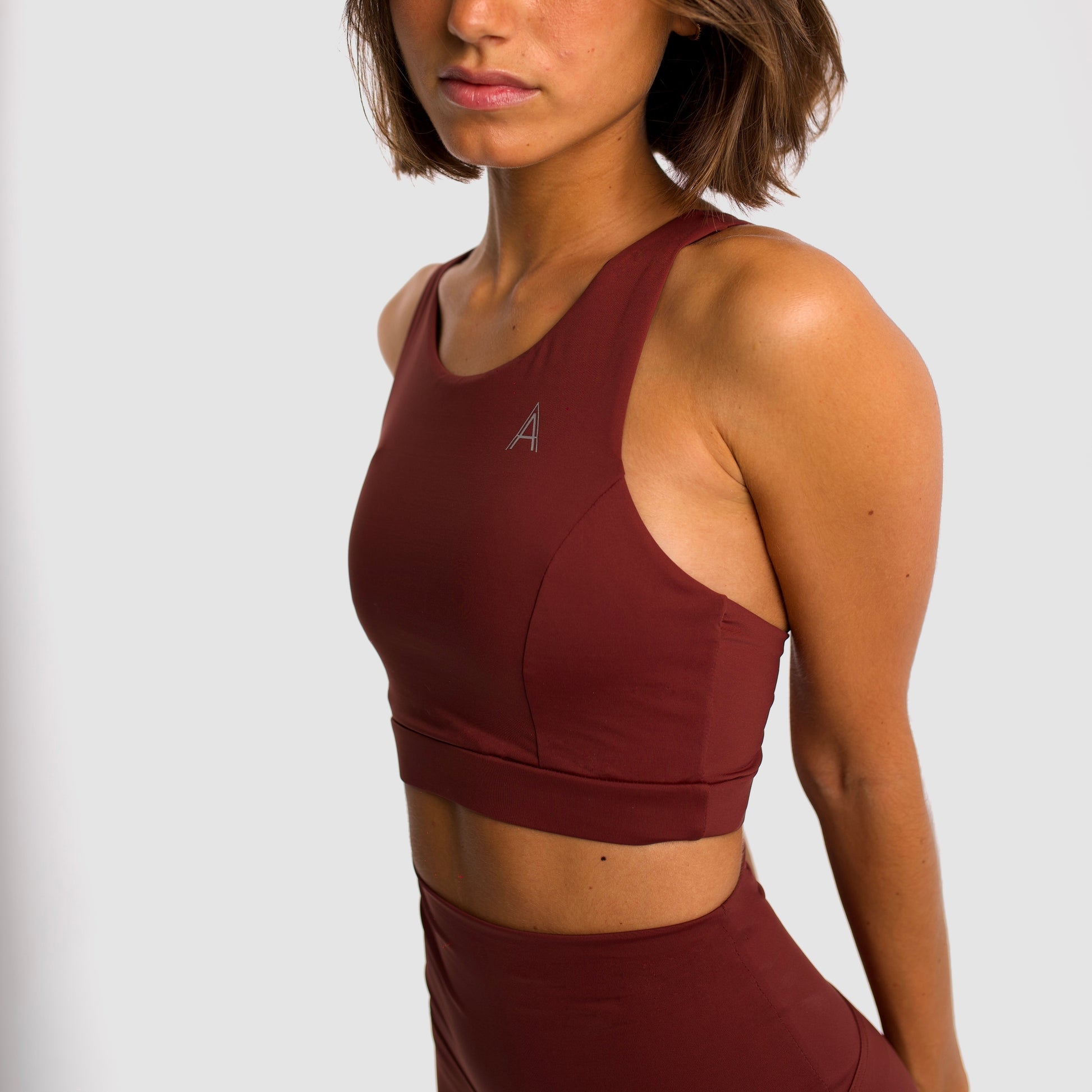 Women's maroon sports top. Long cut bra. Elastic chest strap for comfort and support. Lightweight, breathable and comfortable bra. Removable cups. Top deportivo de mujer color granate. Sujetador de corte largo. Tira elástica en el pecho ofreciendo comodidad y sujeción. Sujetador cómo, ligero y transpirable. Top con copas extraibles. 